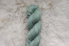 A skein of naturally dyed, light grey yarn lays on a sheepskin rug, and is pictured from above.