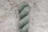 A skein of yarn has been naturally dyed a light grey. It lays on a sheepskin rug.