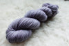 A hand dyed skein of light purple yarn lays on a wool background.