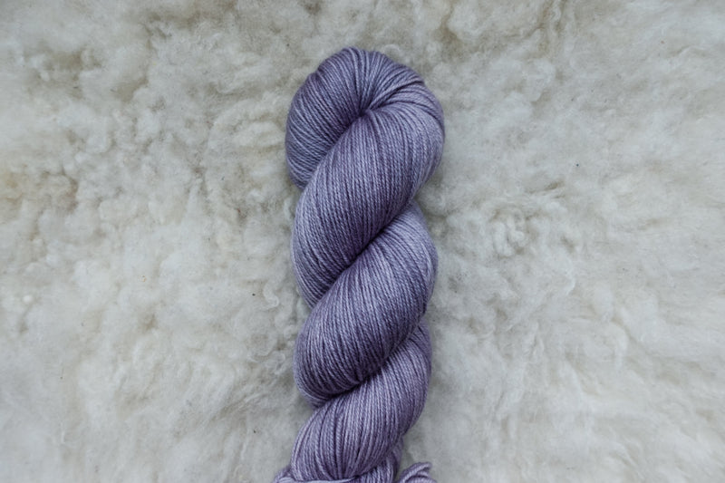 A light purple skein of natural fiber, fingering weight yarn is pictured from above.