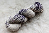 A skein of DK weight yarn has been hand dyed purple and white. It lays on a wool background.
