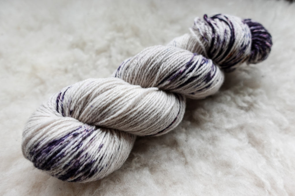 A hand dyed skein of purple and white variegated yarn lays on a tabletop.