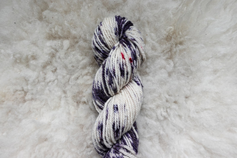 A naturally dyed skein of purple and white variegated yarn is pictured from above.
