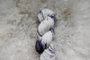 A variegated skein of purple and white, hand dyed yarn is pictured from above.