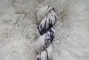 A naturally dyed skein of purple and white variegated yarn is pictured from above, laying on a wool background.