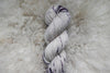 A skein of sport weight yarn has been naturally dyed purple and white. It's pictured from above.