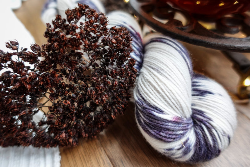 A purple and white skein of naturally dyed yarn sits on a tabletop. Dried flowers lay next to it.