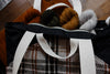 A black canvas and orange and white flannel project bag lays on its. Four skeins of yarn are inside. The bag has two small handles and two longer tote handles.