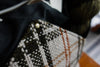A close up of the orange and white handwoven flannel on the exterior of the yarn project bag. Its sewn with black canvas to create a triangle shape.