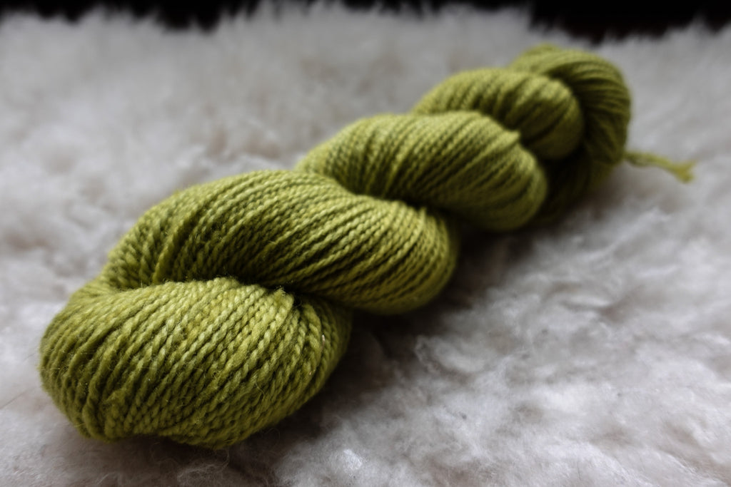 A skein of natural yarn has been hand dyed a bright green. It lies on top of a sheepskin.