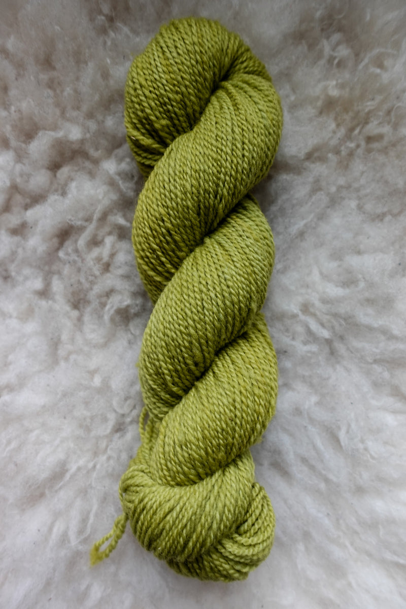 Seen from above, a bright green skein of hand dyed yarn lays on a sheepskin.