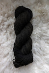 Seen from above a dark, almost black, skein of hand dyed yarn lays on a sheepskin.