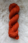 Seen from above, an orange-red skein of hand dyed yarn lays on a sheepskin.