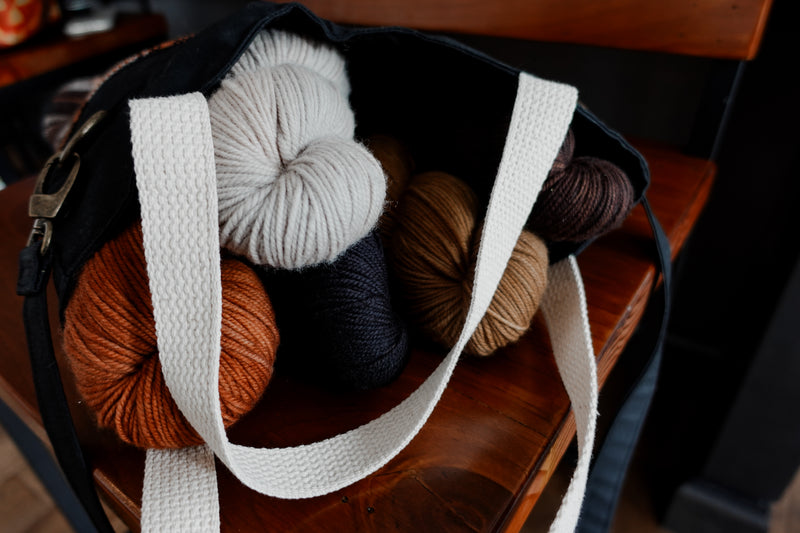 The black canvas and orange flannel tote project bag is open, with five skeins of yarn inside.
