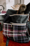 Seen at a three quarter view, a black canvas and purple flannel tote project bag sits on a chair. It has two skeins in the front zippered pockets, one in each.