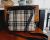 Seen from the back, a knitting project bag sits on a chair. It's made of black canvas and orange, white, and black flannel. It has a long black canvas strap attached with bronze lobster clasps.