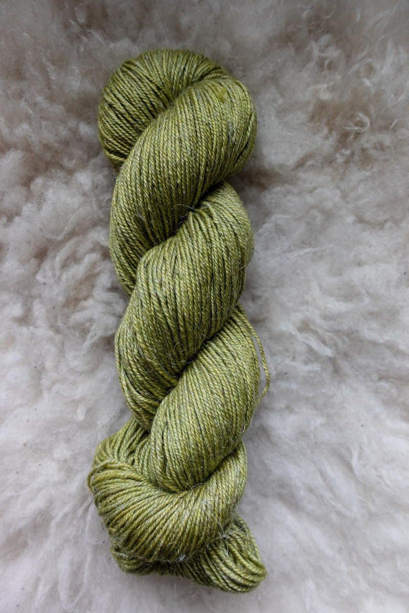 Seen from above, a bright green skein of hand dyed yarn lays on a sheepskin.