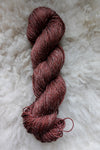 Seen from above, a brick red skein of naturally dyed yarn lays on a sheepskin.