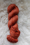 Seen from above, an orange-red skein of naturally dyed yarn lays on a sheepskin.