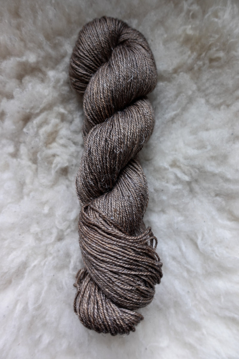 Seen from above, a light brown skein of hand dyed yarn lays on a sheepskin.
