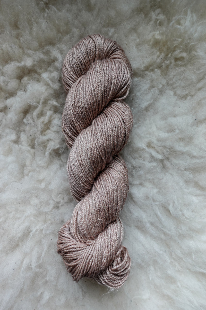 Seen from above, a light pink-beige skein of naturally dyed yarn lays on a sheepskin.