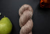 Seen close up, a light pink-beige skein of hand dyed yarn lays on a black surface next to an orange-red flower and a pear.