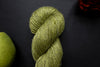 Seen close up, a bright green skein of yarn lays on a black surface next to an orange-red flower and a pear.