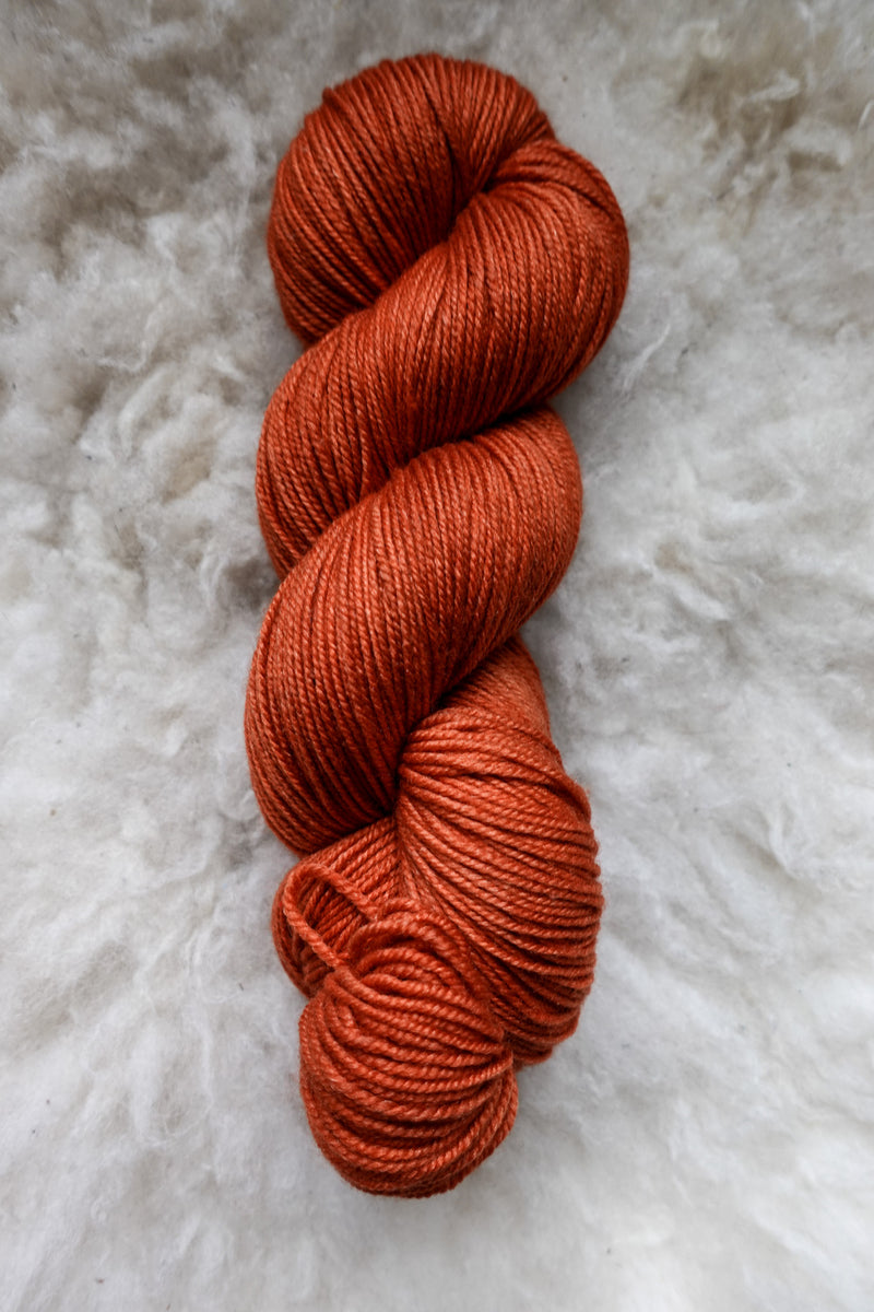 Seen from above, an orange-red skein of hand dyed yarn lays on a sheepskin.