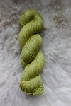 A skein of yarn, naturally dyed bright green, is seen from above and lays on a sheepskin.
