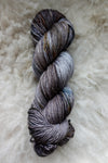 Seen from above, a variegated skein of brown, grey, and white naturally dyed yarn lays on a sheepskin.