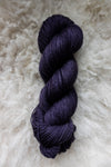 Seen from above, a deep purple skein of naturally dyed yarn lays on a sheepskin.