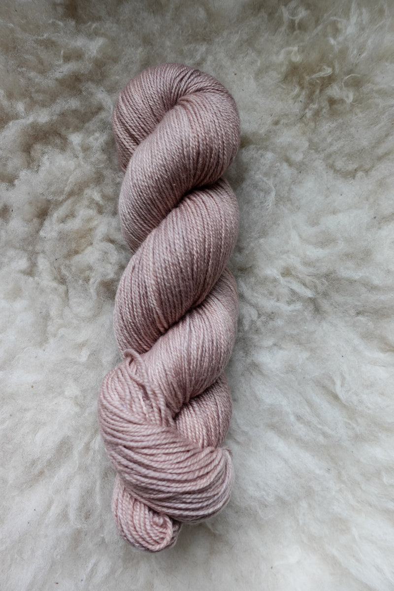Seen from above, a light pink-beige skein of naturally dyed yarn lays on a sheepskin. 