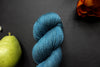Seen close up, an indigo blue skein of hand dyed yarn lays on a black surface next to an orange-red flower and a pear.