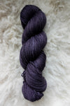 Seen from above, a deep purple skein of hand dyed yarn lays on a sheepskin.