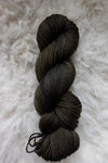 Seen from above, a dark, almost black skein of hand dyed yarn lays on a sheepskin.
