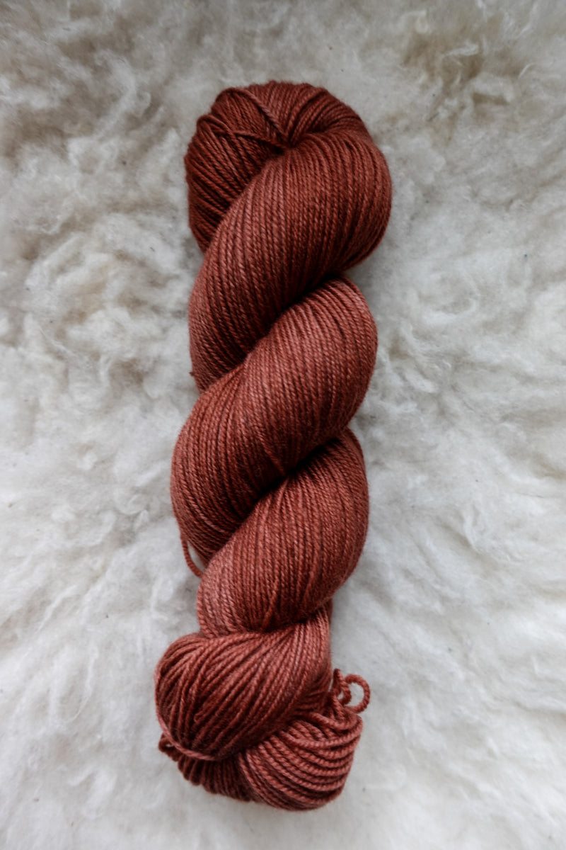 Seen from above, a brick red skein of naturally dyed skein lays on a sheepskin.
