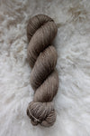 Seen from above, a light brown skein of naturally dyed yarn lays on a sheepskin.