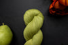Seen from above, a bright green skein of naturally dyed yarn lays on a black surface next to an orange-red flower and a pear.