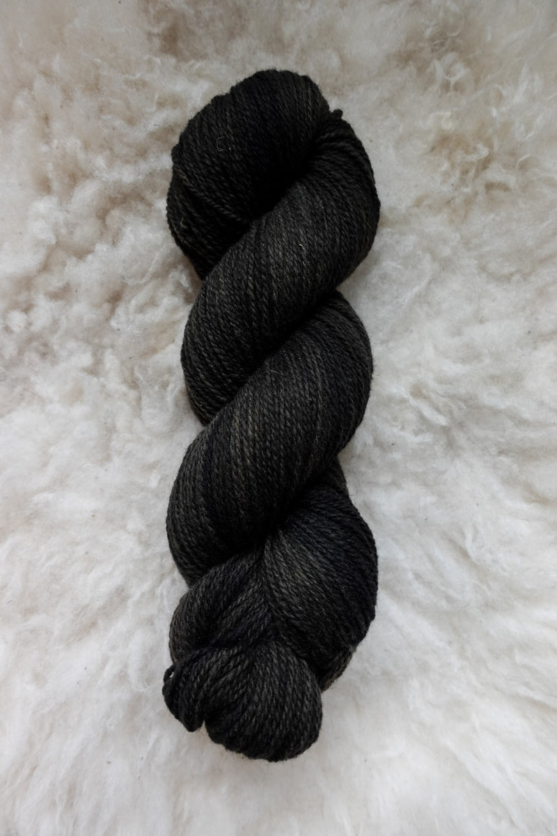 Seen from above, a dark, almost black, skein of naturally dyed yarn lays on a sheepskin.
