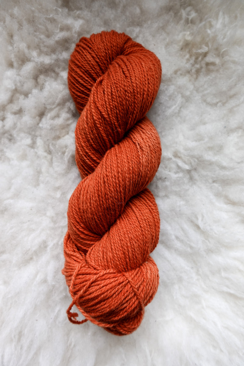 Seen from above, an orange-red skein of naturally dyed lays on a sheepskin.