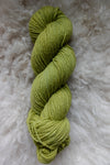 A bright green skein of hand dyed yarn is seen from above, laying on a sheepskin.