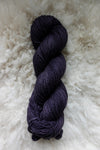 Seen from above, a naturally dyed skein of deep purple yarn lays on a sheepskin.