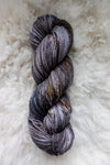 Seen from above, a variegated skein of brown, grey, and white hand dyed yarn lays on a sheepskin.